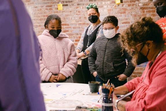 A group of people watch an artist paint.