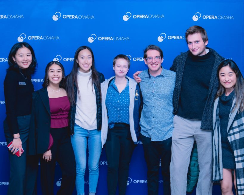 Bảy thành viên Weitz đang mỉm cười trước ống kính và đứng trước phông nền Opera Omaha màu xanh lam.